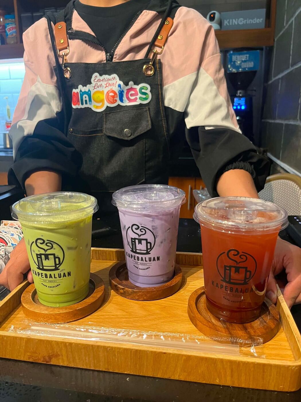 A barista presenting a tray of matcha, taro, and fruit tea Kapebaluan drinks