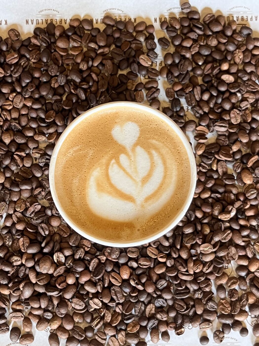 A latte with tulip art nestled in a bed of fresh roasted beans