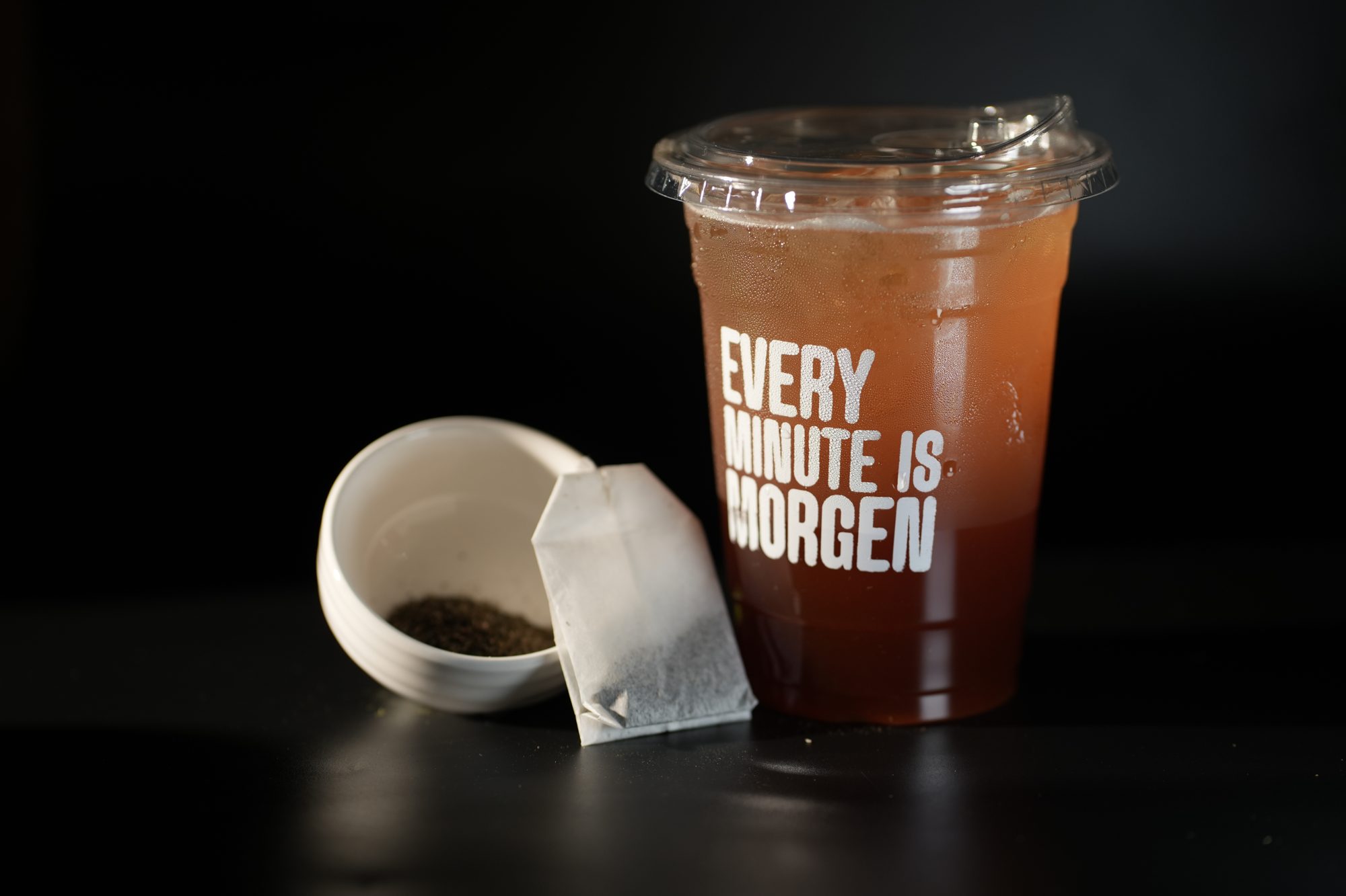 An amber iced tea in an Every Minute is Morgen cup with loose tea leaves
